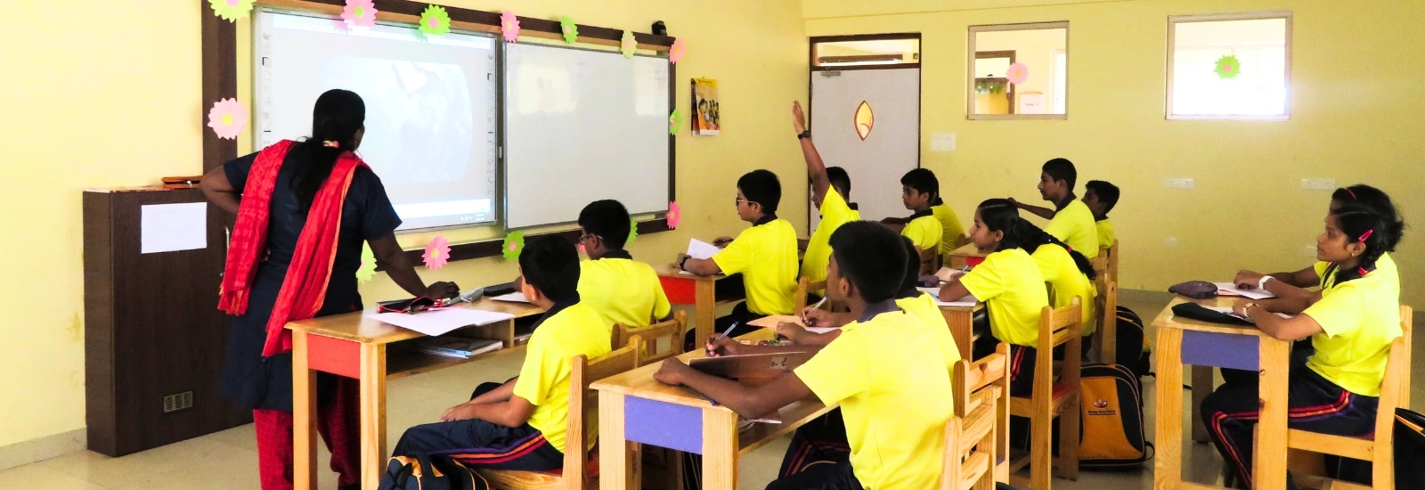 Students at NewAge World School engaged in an interactive classroom session with a teacher using a digital smart board for enhanced learning.